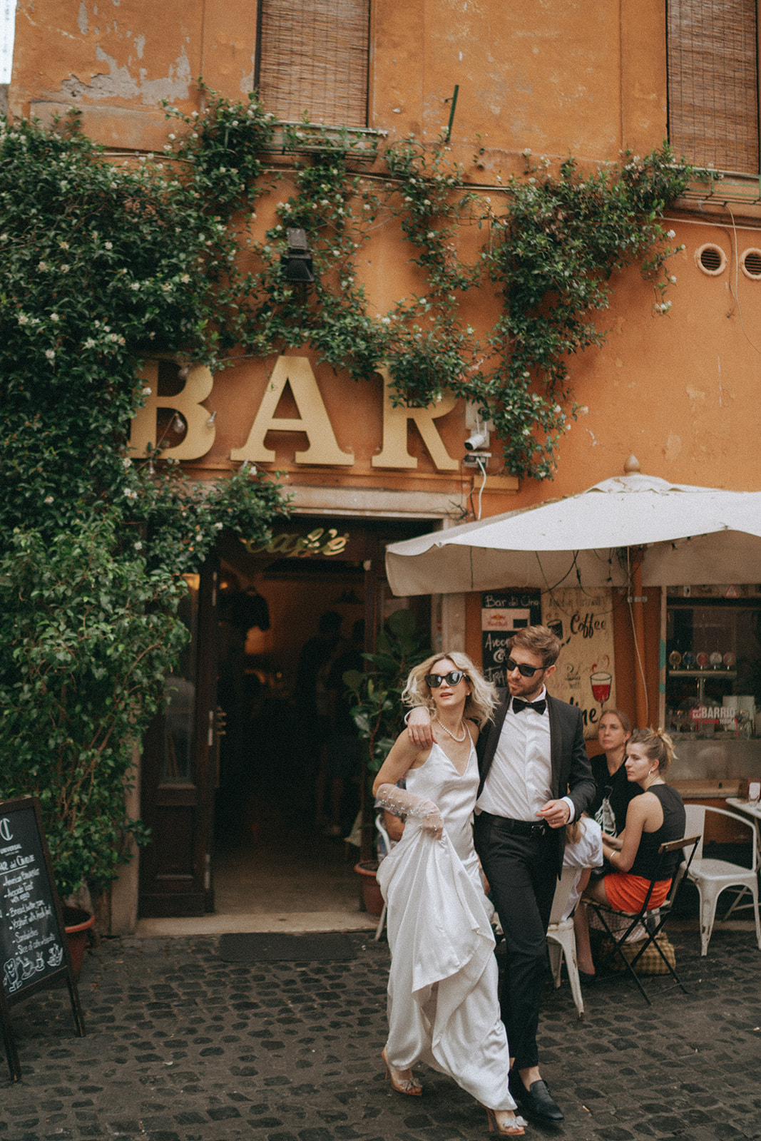 Bride and groom walk out of a small Trastevere coffee shop by Rome elopement photographer Elsie Goodman.