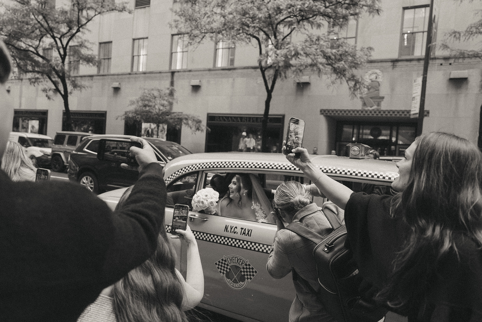 Madison + Dylan 620 Loft and Garden Wedding bride with head out of vintage taxi window with people taking photos after 620 loft & garden wedding, shot by elsie goodman, a destination and NYC wedding photographer