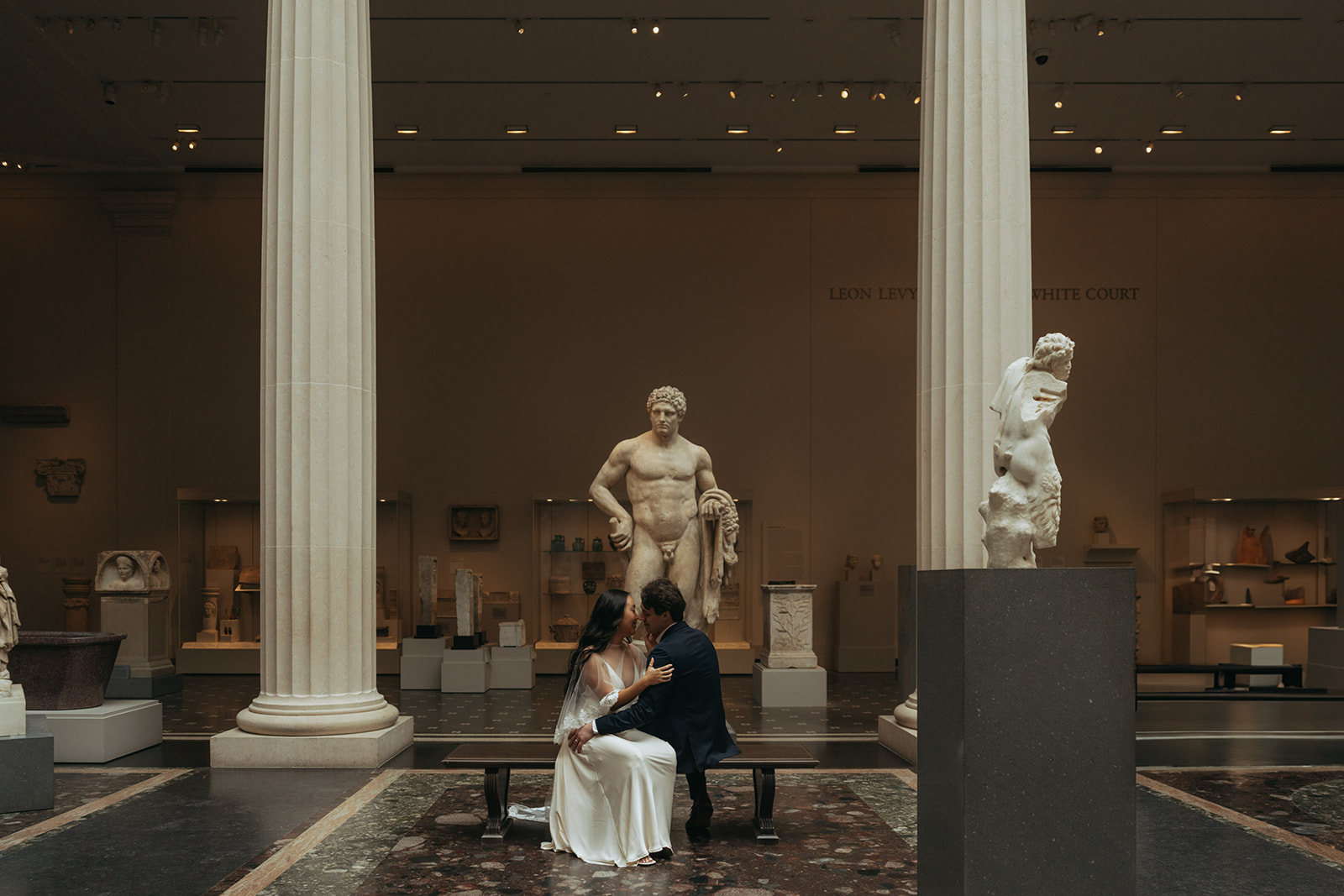 Alex + Bardo NYC Elopement Photos bride and groom sitting on bench at the Met in front of sculptures for elopement photos, shot by elsie goodman, a destination, wedding and NYC elopement photographer