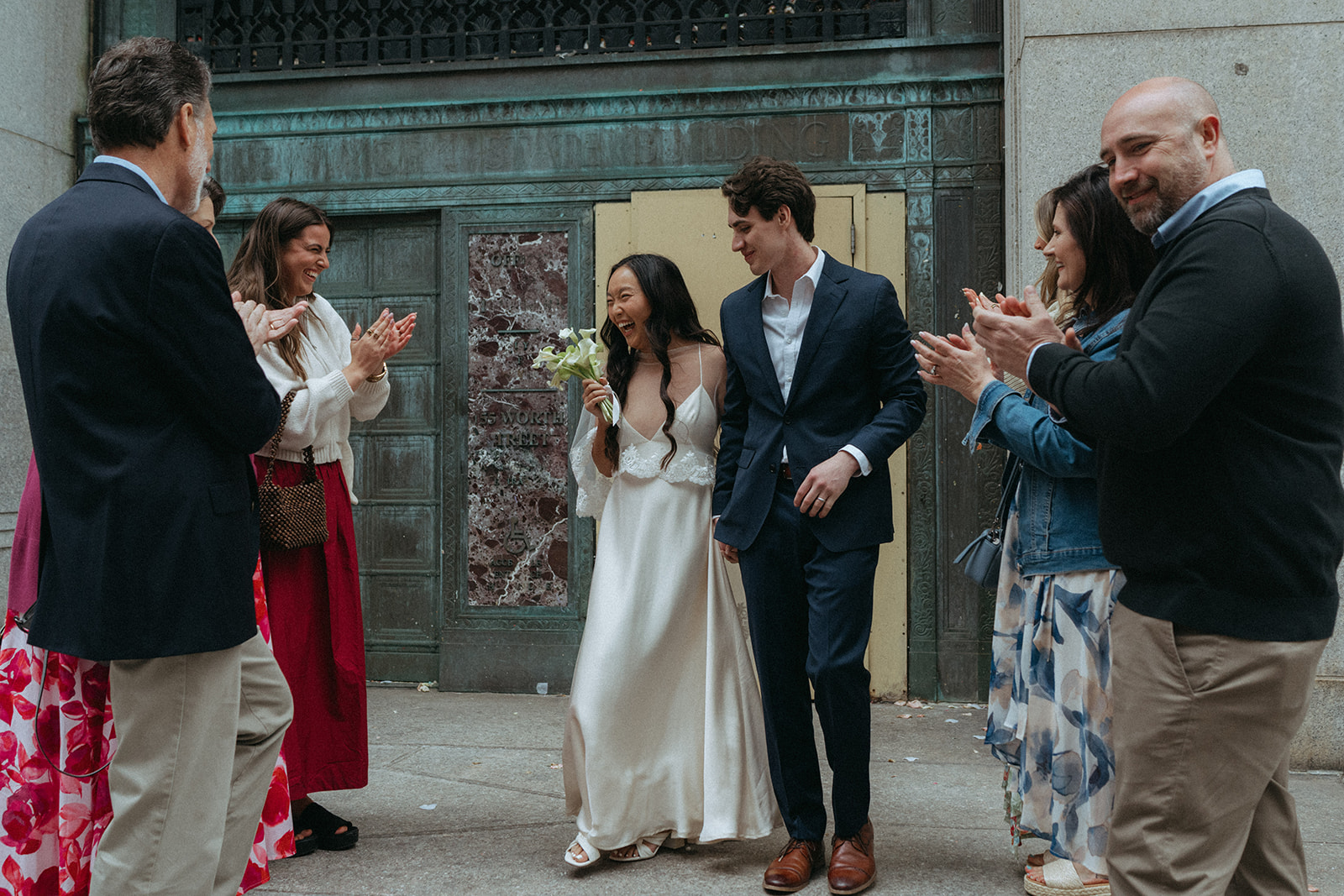 Alex + Bardo NYC Elopement Photos bride and groom coming out of nyc city hall after getting married to loved ones clapping, shot by elsie goodman, a destination, wedding and NYC elopement photographer