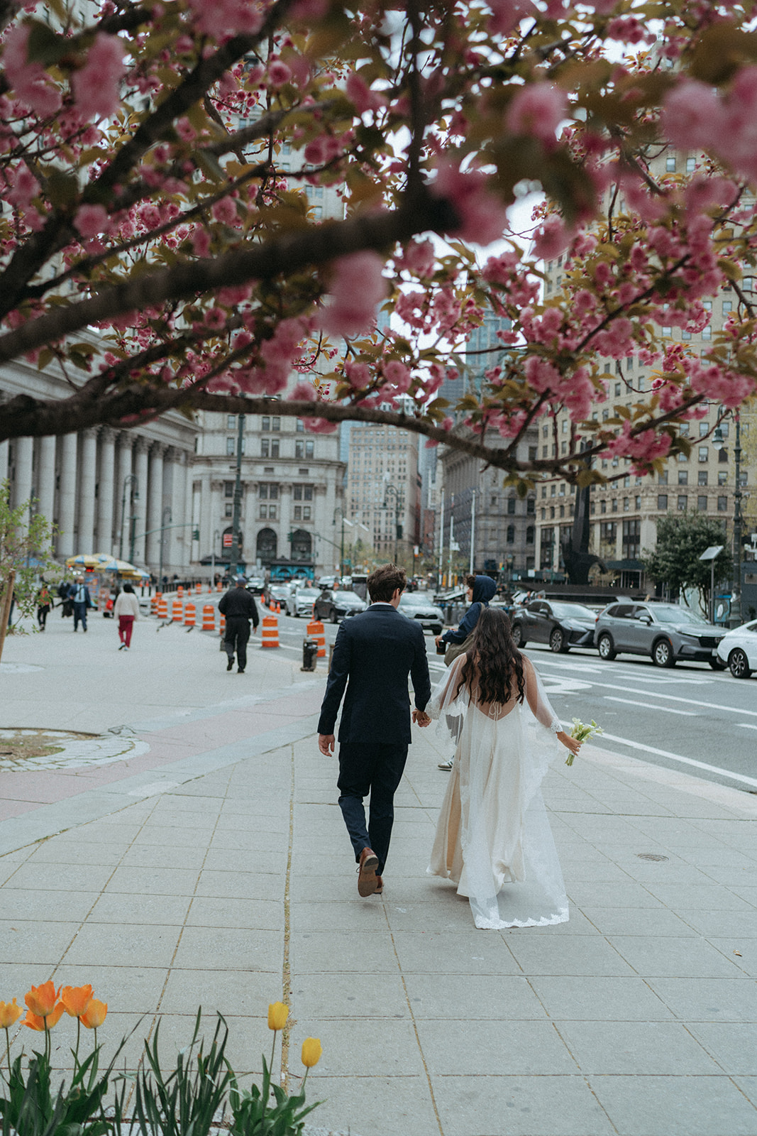Alex + Bardo NYC Elopement Photos bride and groom walking under cherry blossoms in nyc after eloping, shot by elsie goodman, a destination, wedding and NYC elopement photographer