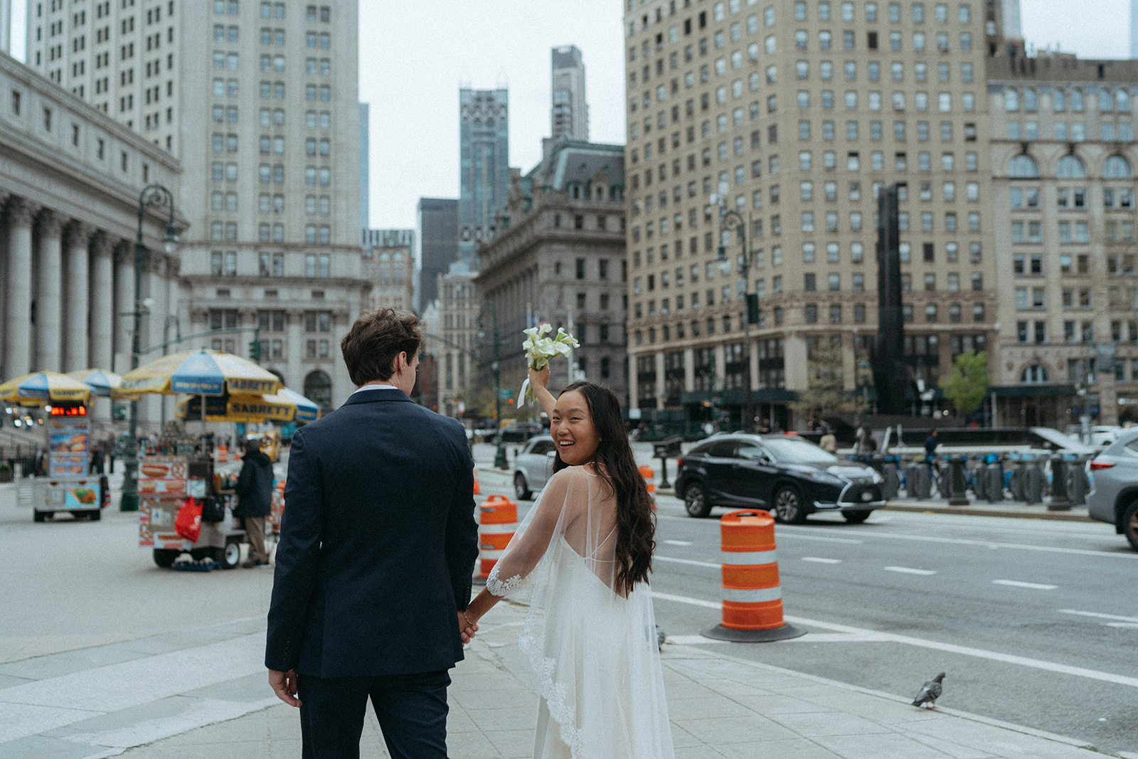 Alex + Bardo NYC Elopement Photos bride and groom walking in nyc after eloping, bride looking over shoulder and holding flowers up, shot by elsie goodman, a destination, wedding and NYC elopement photographer