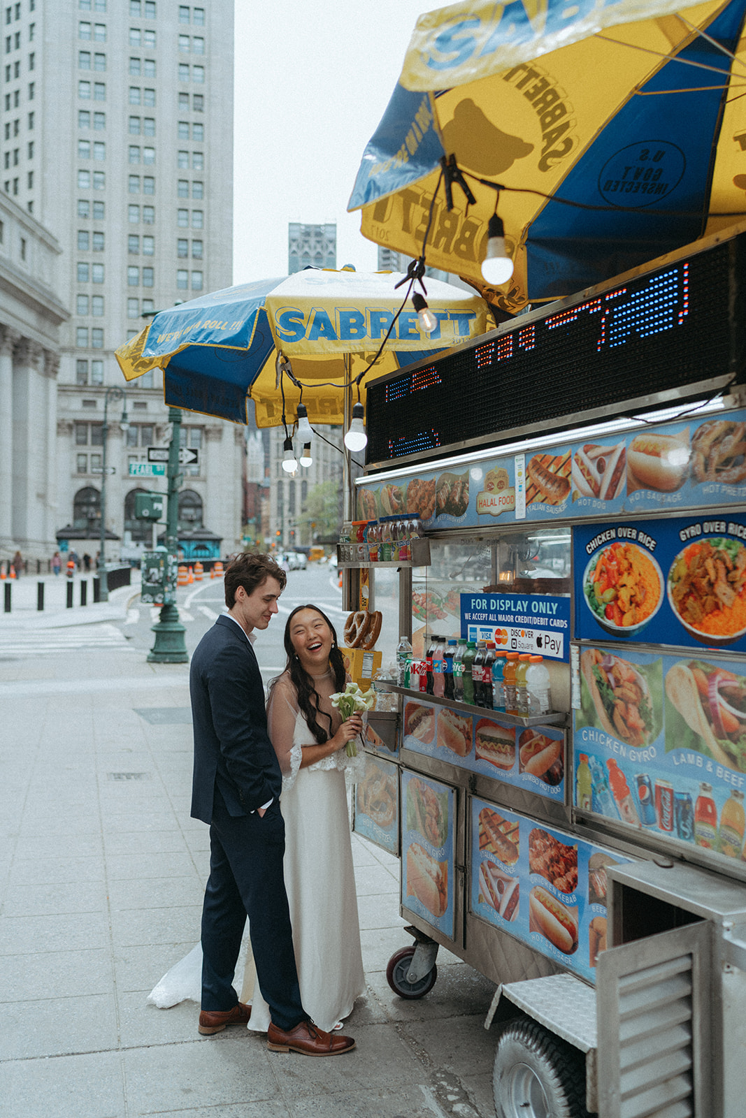 Alex + Bardo NYC Elopement Photos bride laughing with groom while getting hot dogs in nyc after eloping at city hall, shot by elsie goodman, a destination, wedding and NYC elopement photographer