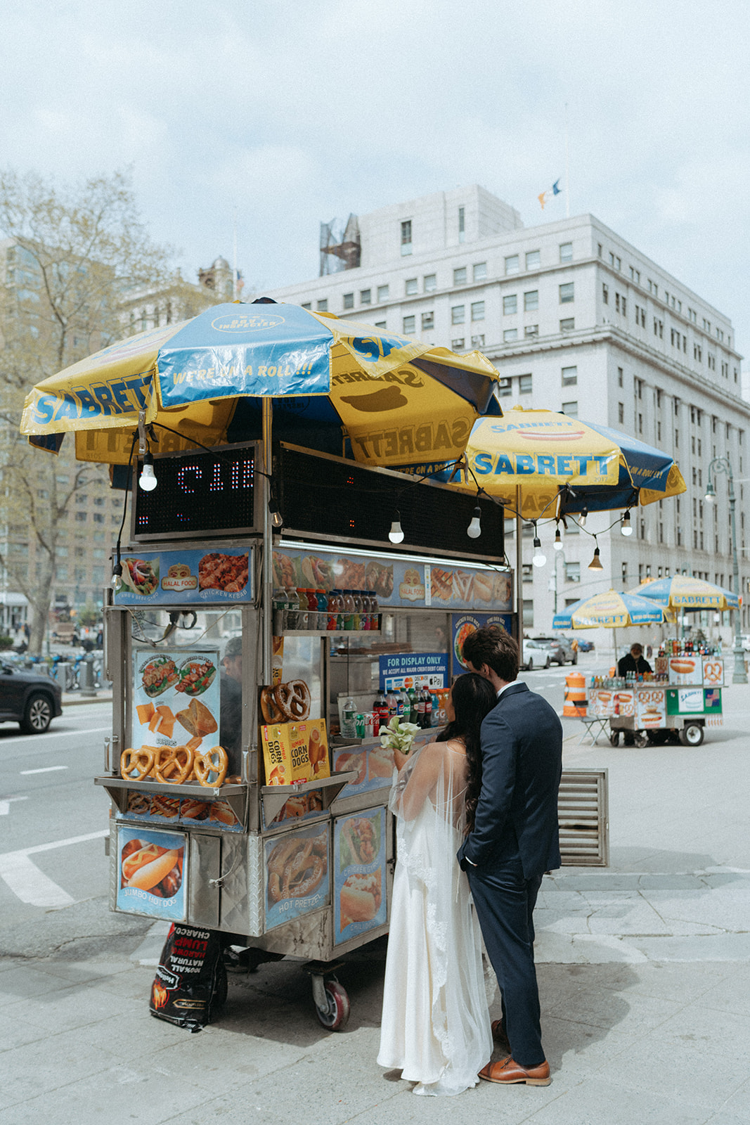 Alex + Bardo NYC Elopement Photos bride and groom waiting for hot dogs from cart in nyc after eloping at city hall, shot by elsie goodman, a destination, wedding and NYC elopement photographer