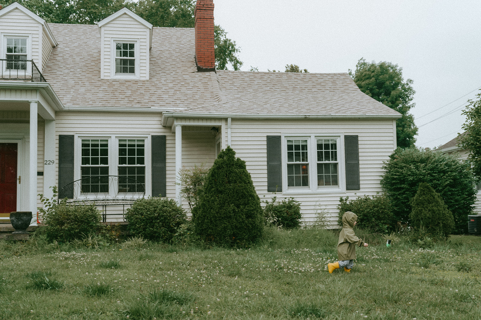 Child running across a lawn in a rain coat and yellow rain boots by maternity, family, and wedding photographer Elsie Goodman.