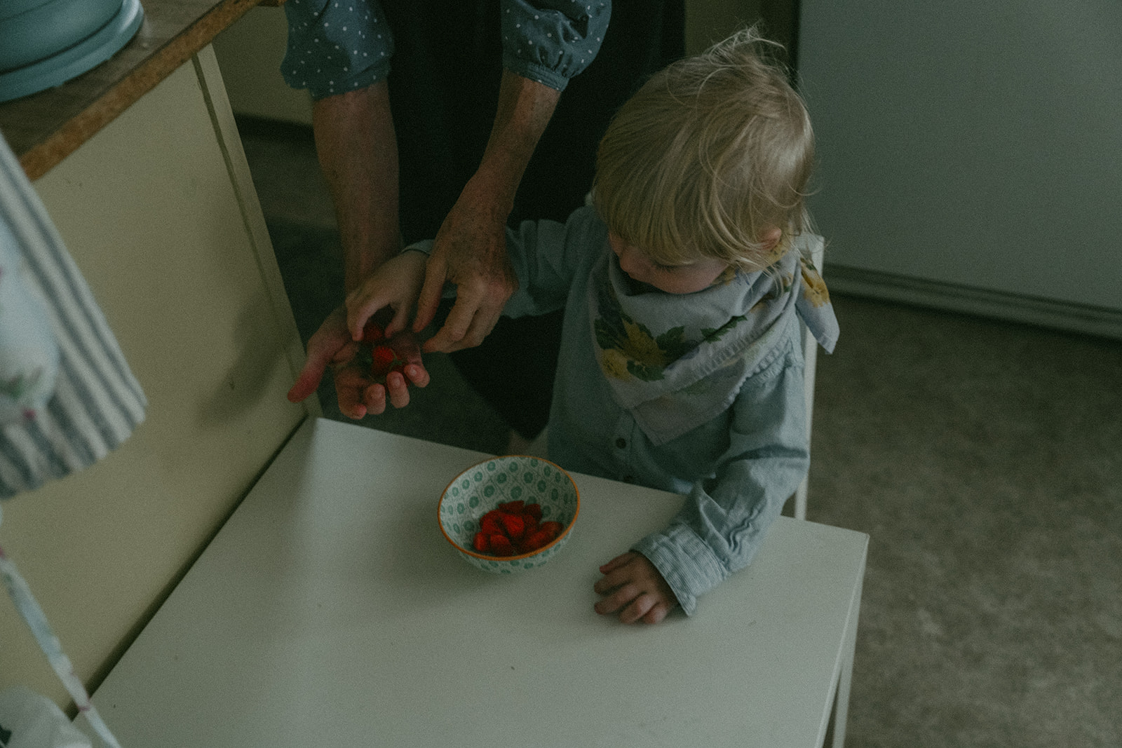 Dad helping his son with some strawberries in the kitchen by maternity, family, and wedding photographer Elsie Goodman.