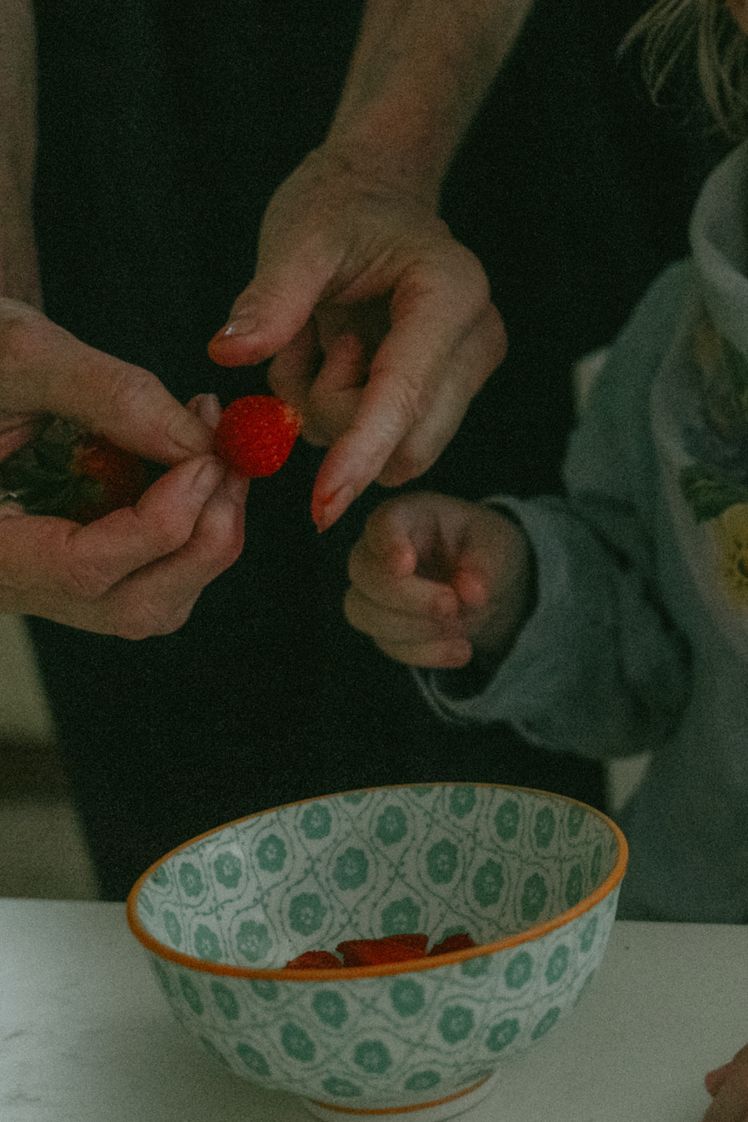 Mom helps her child with strawberries in the kitchen by maternity, family, and wedding photographer Elsie Goodman.