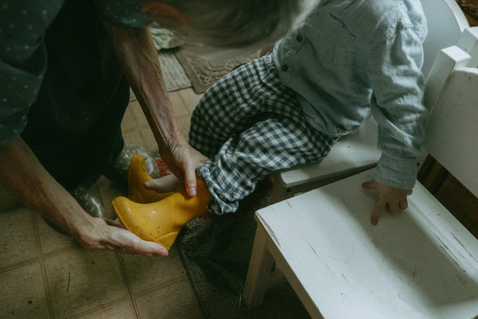 Person helps take off a child's rain boots by maternity, family, and wedding photographer Elsie Goodman.