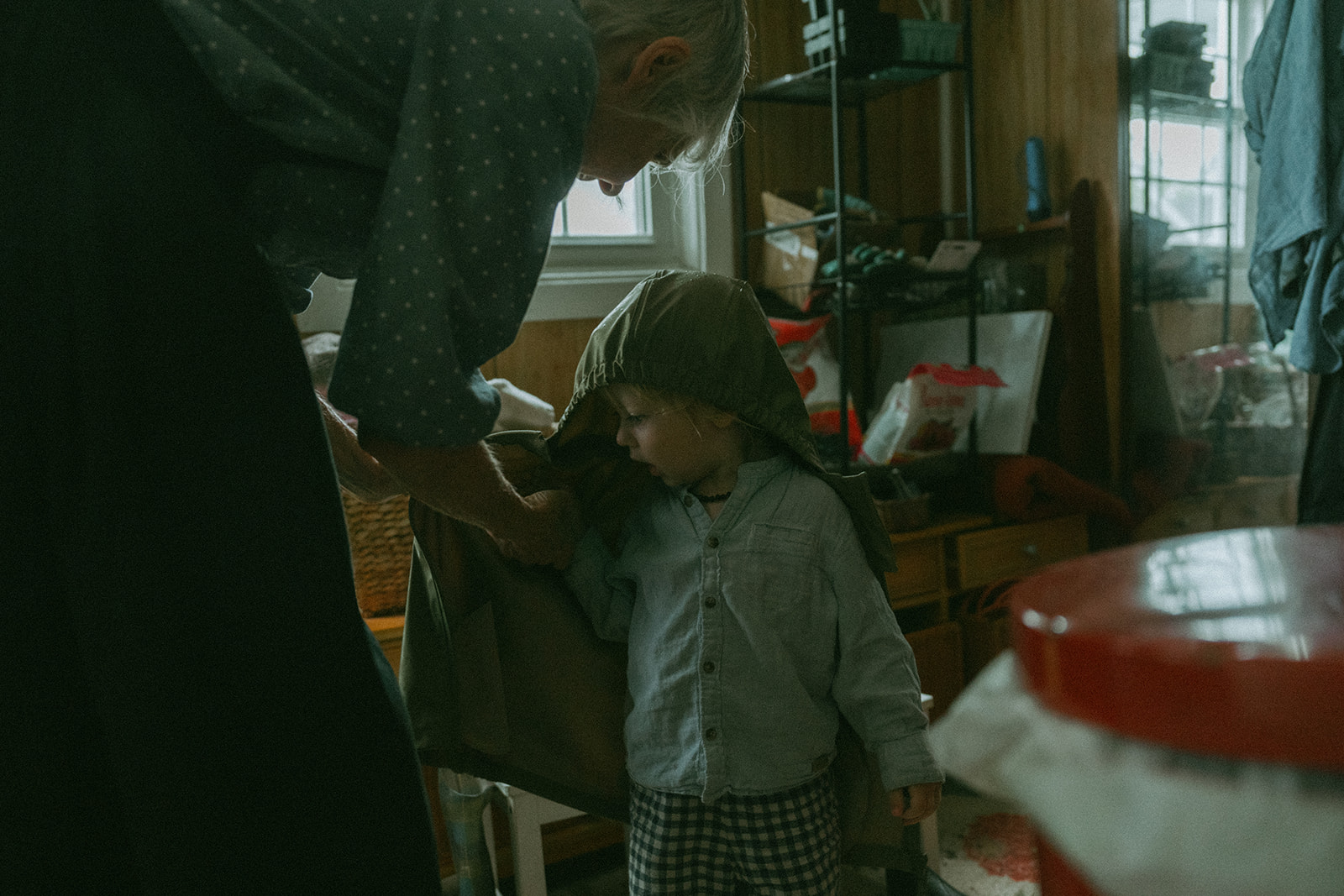Care taker helps take off a child rain jacket by maternity, family, and wedding photographer Elsie Goodman.