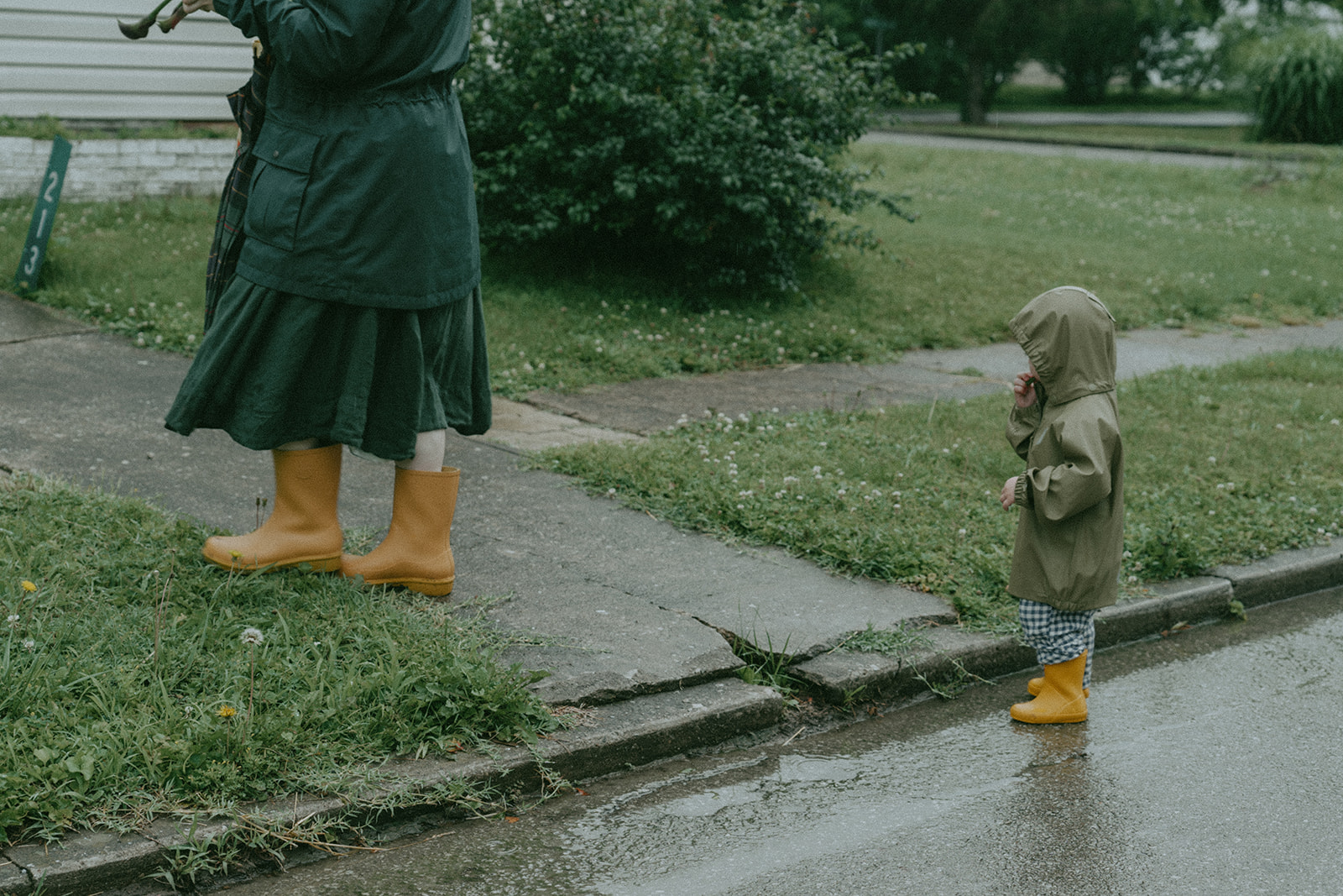 Child stands on a wet street with mom in matching yellow rain boots by maternity, family, and wedding photographer Elsie Goodman.