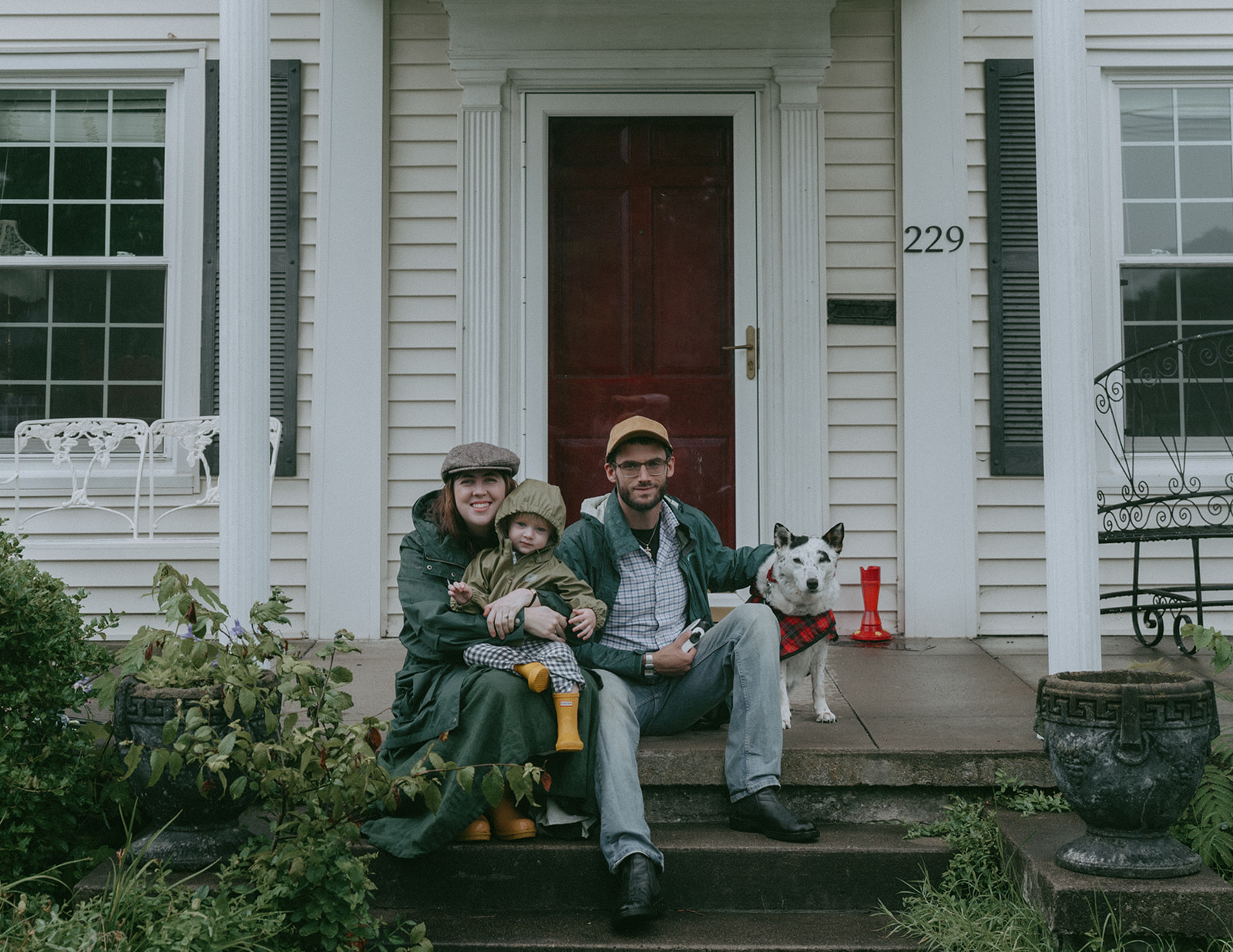 Mom, Dad, child and dog all sit on the front steps of their house by maternity, family, and wedding photographer Elsie Goodman.