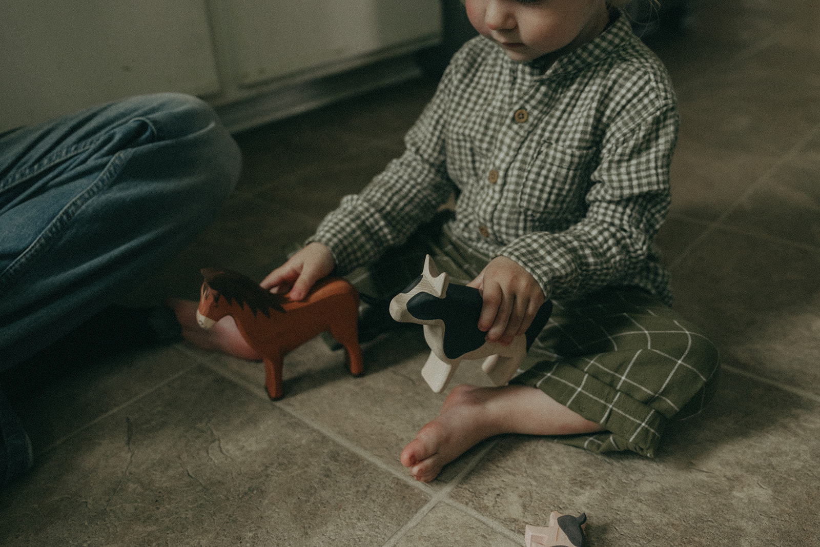 Child sitting on the kitchen floor playing with wooden animal toys by maternity, family, and wedding photographer Elsie Goodman.