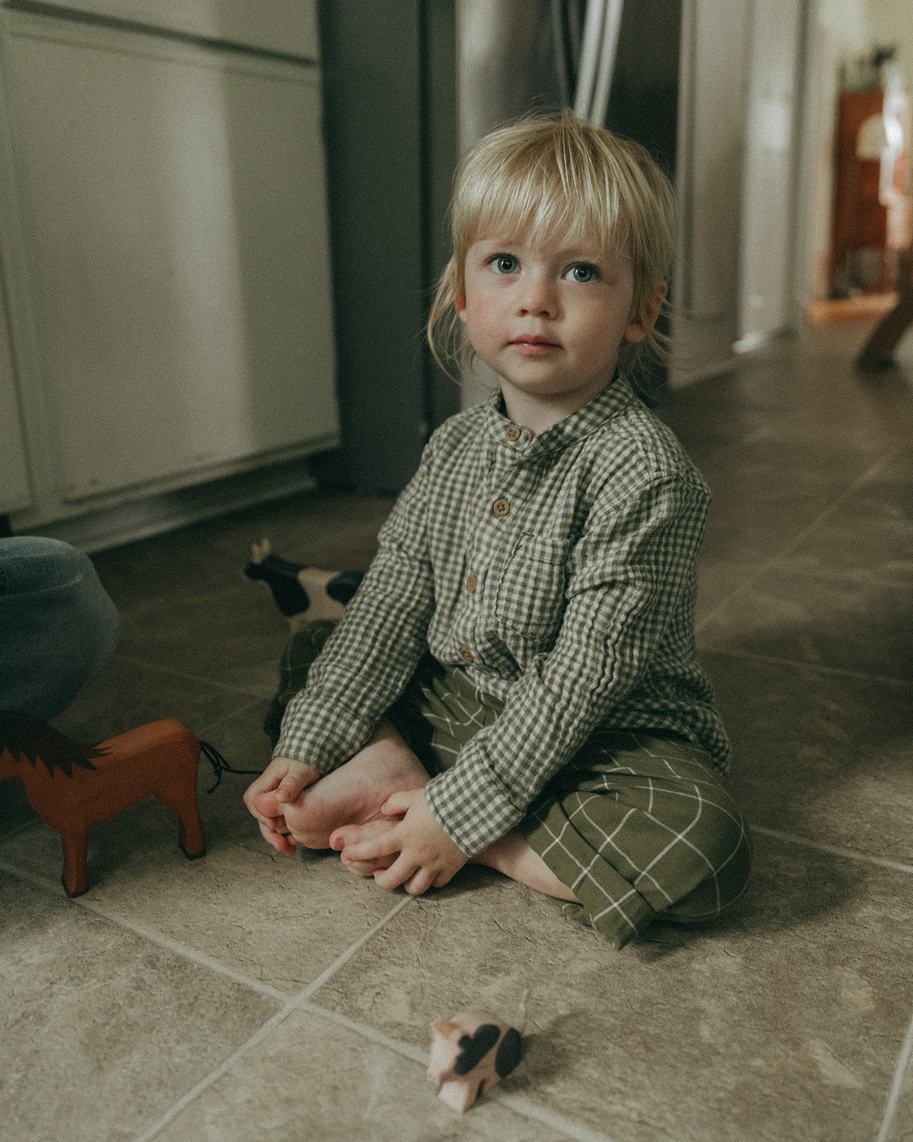 Child sitting on the kitchen floor looking at the camera by maternity, family, and wedding photographer Elsie Goodman.