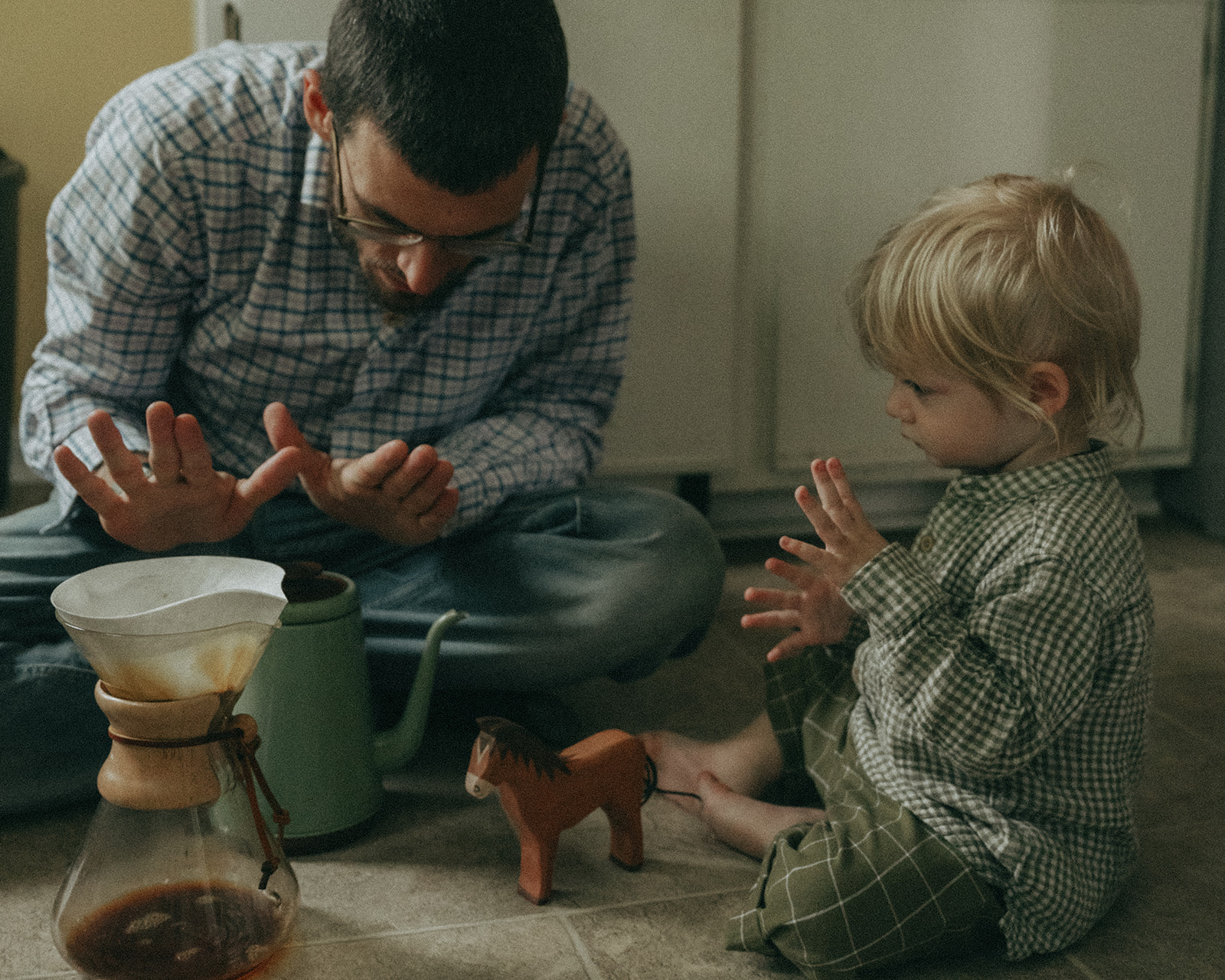 Dad and child sitting on the kitchen floor making coffee in a Chemex by maternity, family, and wedding photographer Elsie Goodman.