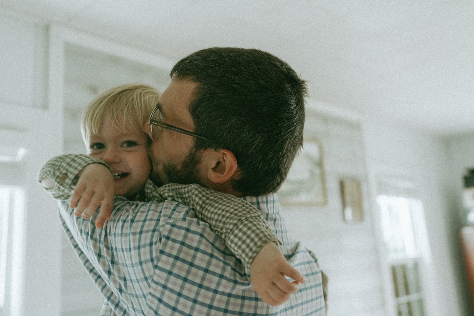 Dad holding up his child giving them a kiss on the cheek by maternity, family, and wedding photographer Elsie Goodman.