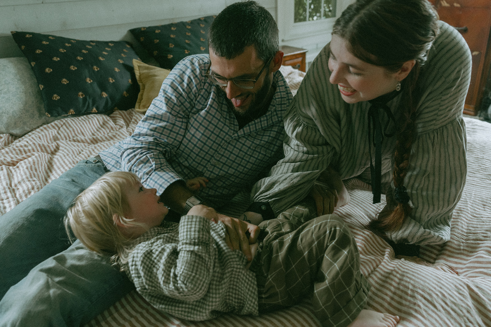Mom, Dad and child laying on the bed together by maternity, family, and wedding photographer Elsie Goodman.