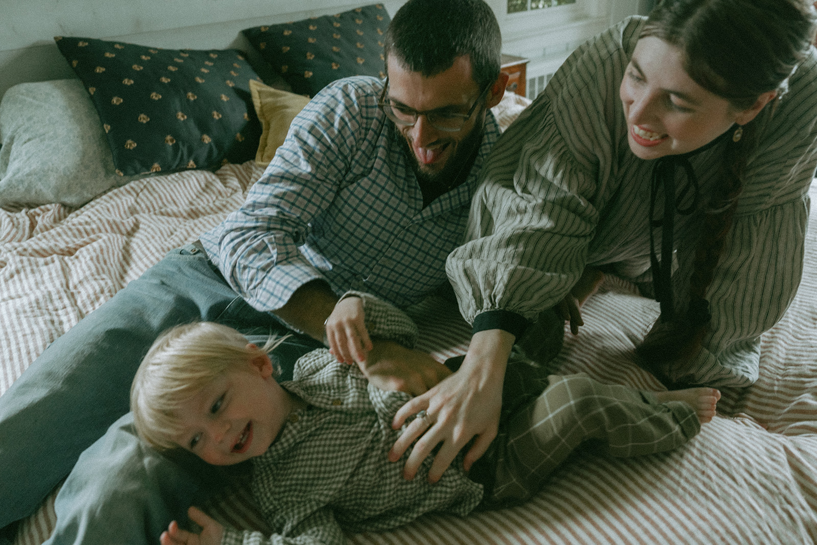 Mom, Dad and child laying on the bed together by maternity, family, and wedding photographer Elsie Goodman.
