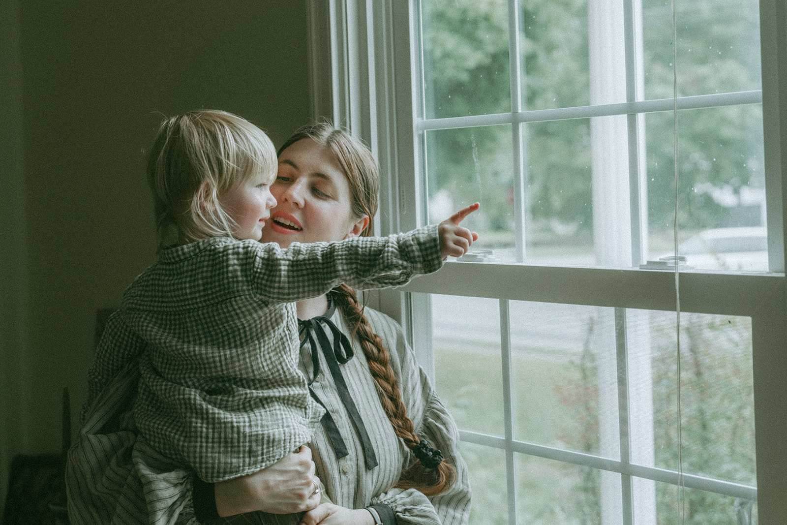 Mom holding child while they point, looking out the window by maternity, family, and wedding photographer Elsie Goodman.