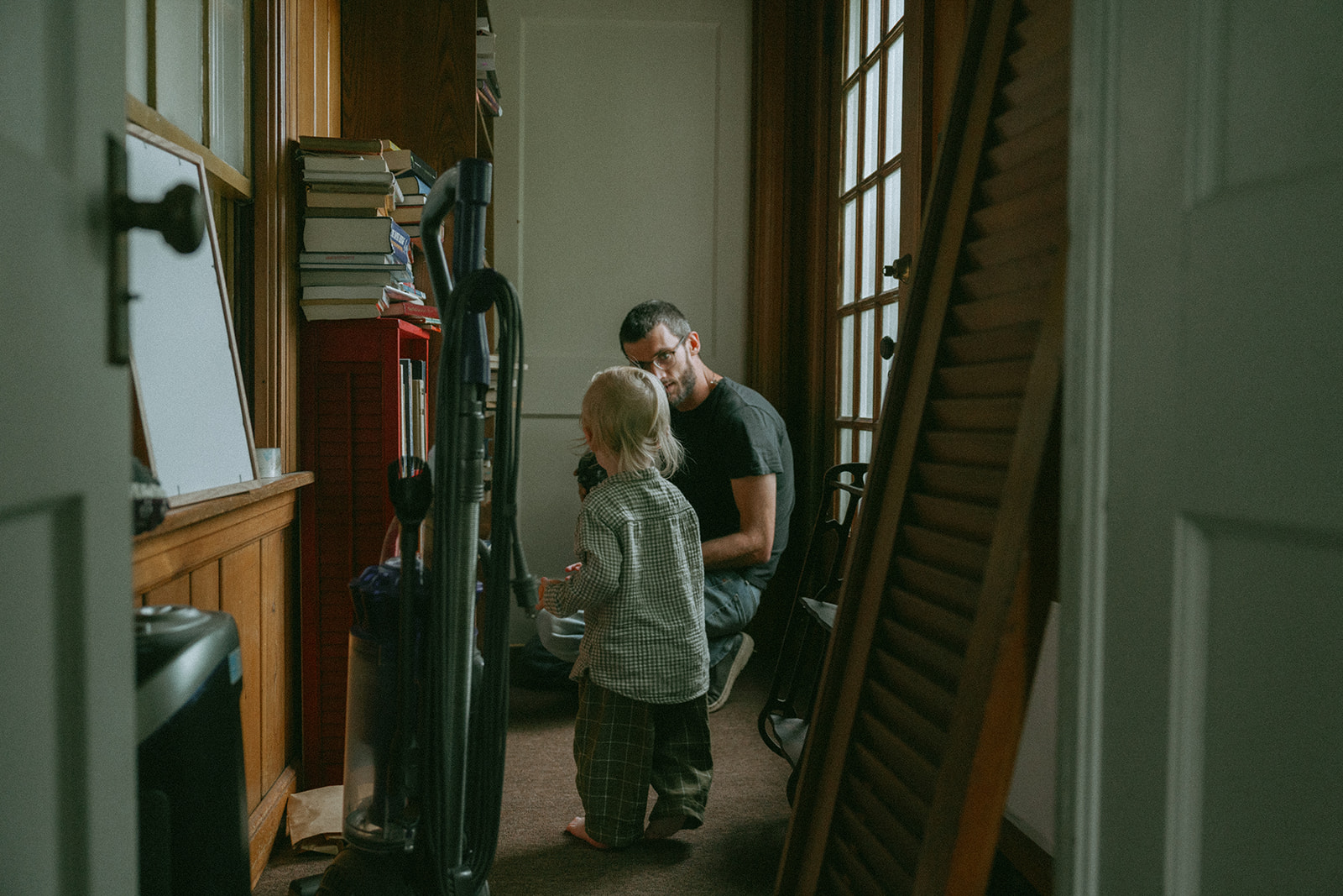 Child standing in the hallway looking at their dad by maternity, family, and wedding photographer Elsie Goodman.