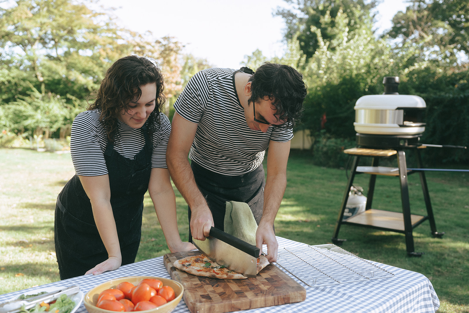Couple cutting a pizza on a wood cutting board in the backyard by couples photographer, Elsie Goodman.