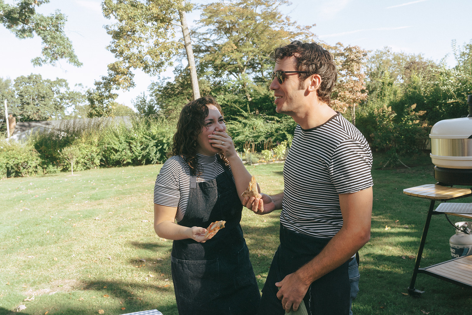 Couple eating a piece of pizza in the backyard laughing, by couples photographer, Elsie Goodman.