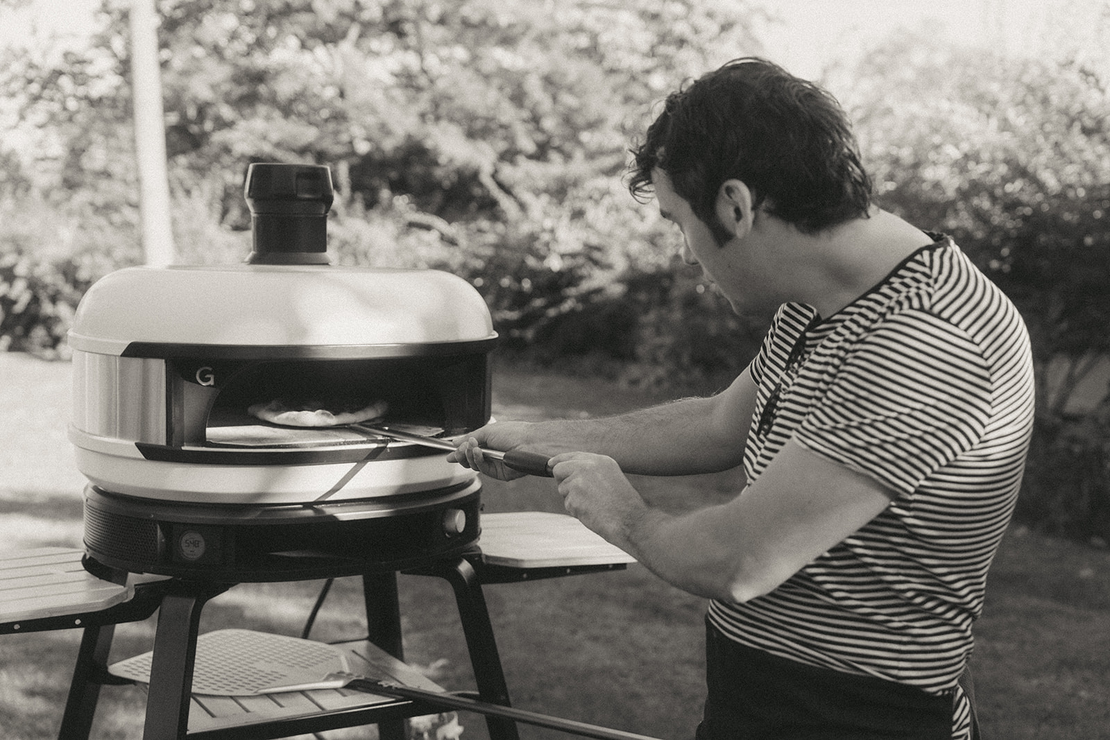 A man putting a pizza in an outdoor pizza oven by couples photographer, Elsie Goodman.