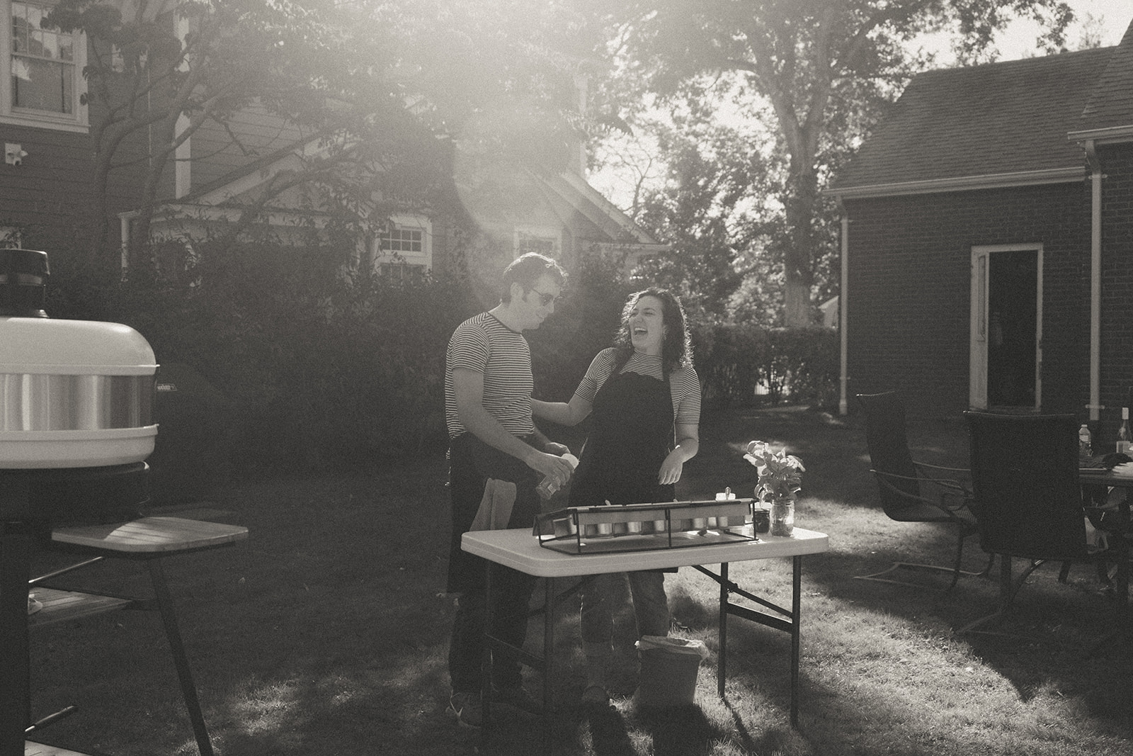 Black and white photo of a couple laughing making pizza in the backyard by couples photographer, Elsie Goodman.