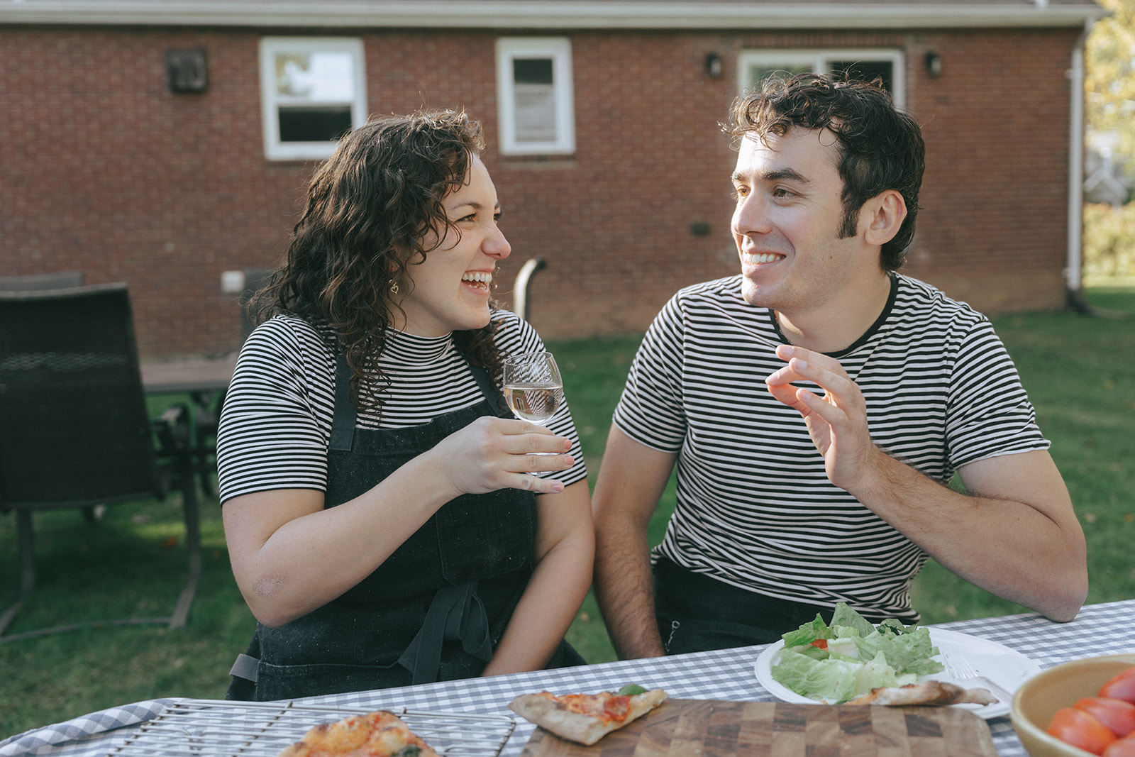 Man and women in matching striped t-shirts enjoying pizza and wine in their backyard by the wedding and couples photographer, Elsie Goodman.