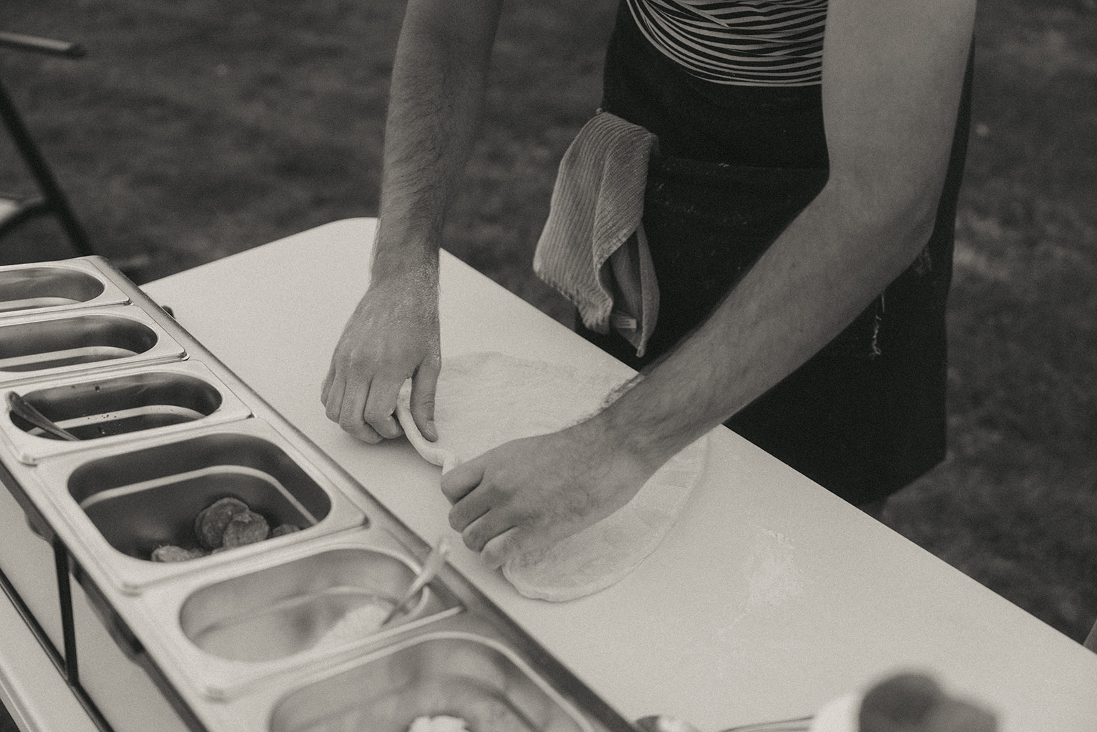 man stretching pizza dough into a heart on a table in the backyard by the wedding and couples photographer, Elsie Goodman.