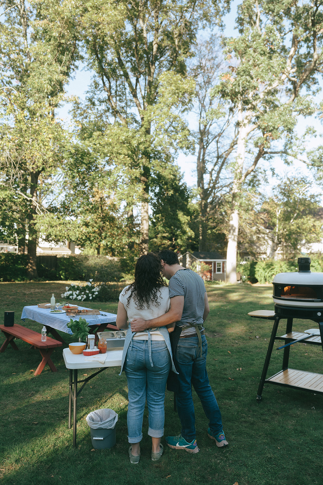 Man with his arm around the waist of his partner while they make pizza in the backyard by the wedding and couples photographer, Elsie Goodman.