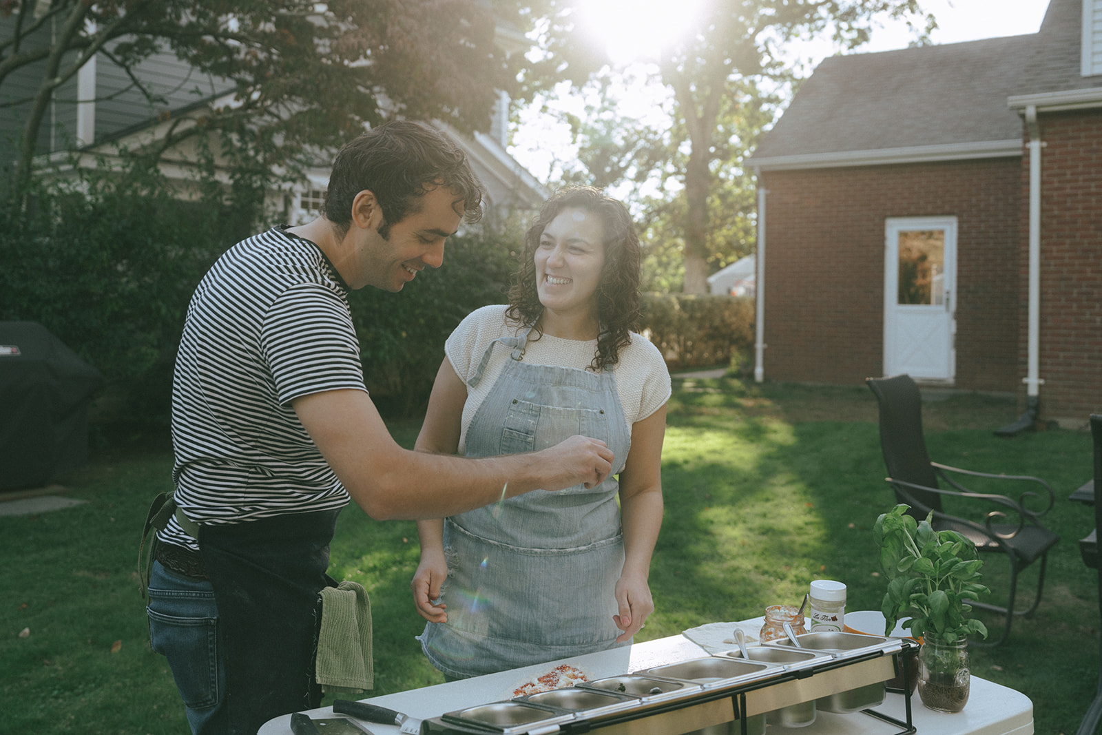A couple smiling while making pizza in the backyard by the wedding and couples photographer, Elsie Goodman.