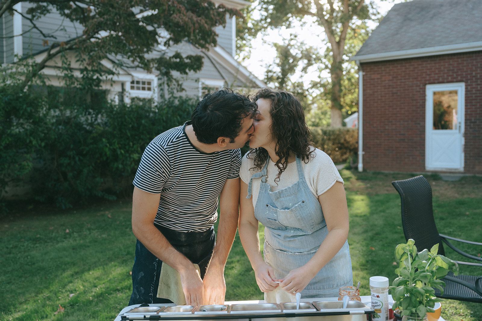 Couple kissing while making pizza outdoors by wedding and couples photographer Elsie Goodman.