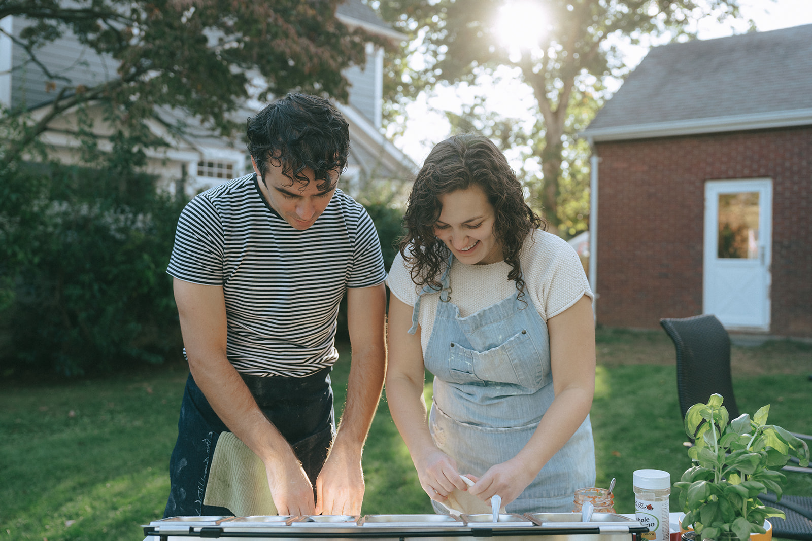 Couple leaning over a table making pizza's outdoors by wedding and couples photographer Elsie Goodman.