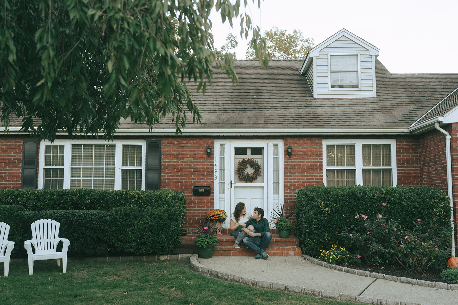 Couple sitting on the front steps of their house looking at each other by wedding and couples photographer Elsie Goodman.