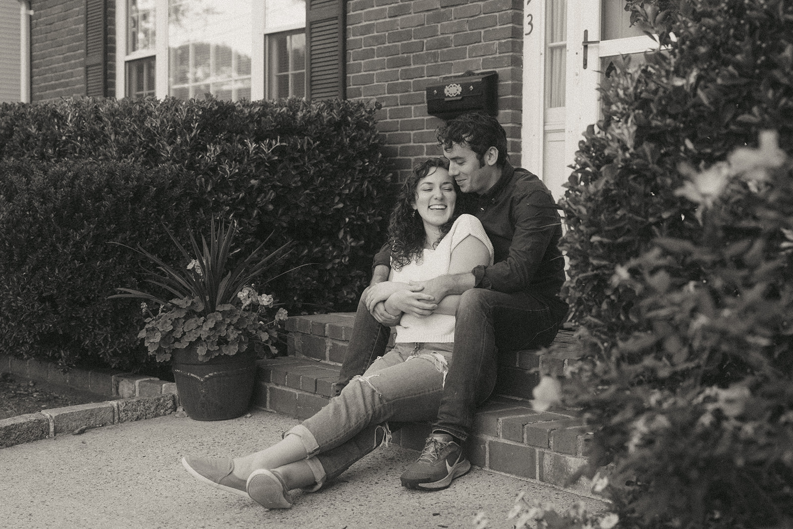 Black and white photo of a couple sitting on the front steps of their house by wedding and couples photographer Elsie Goodman.