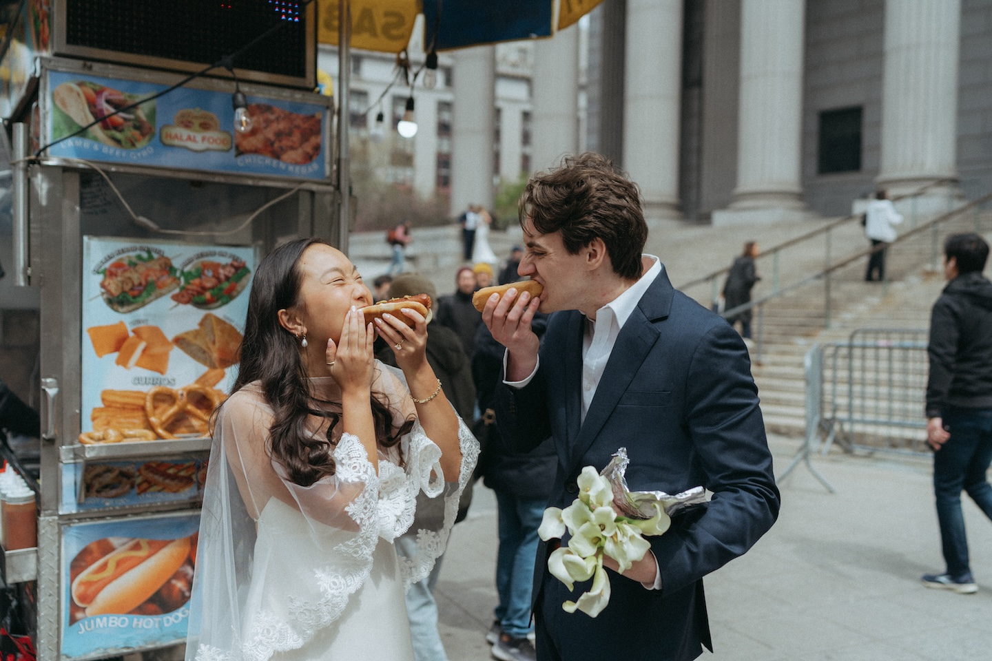 Bride and groom eating hot dogs from a street cart after eloping in New York City