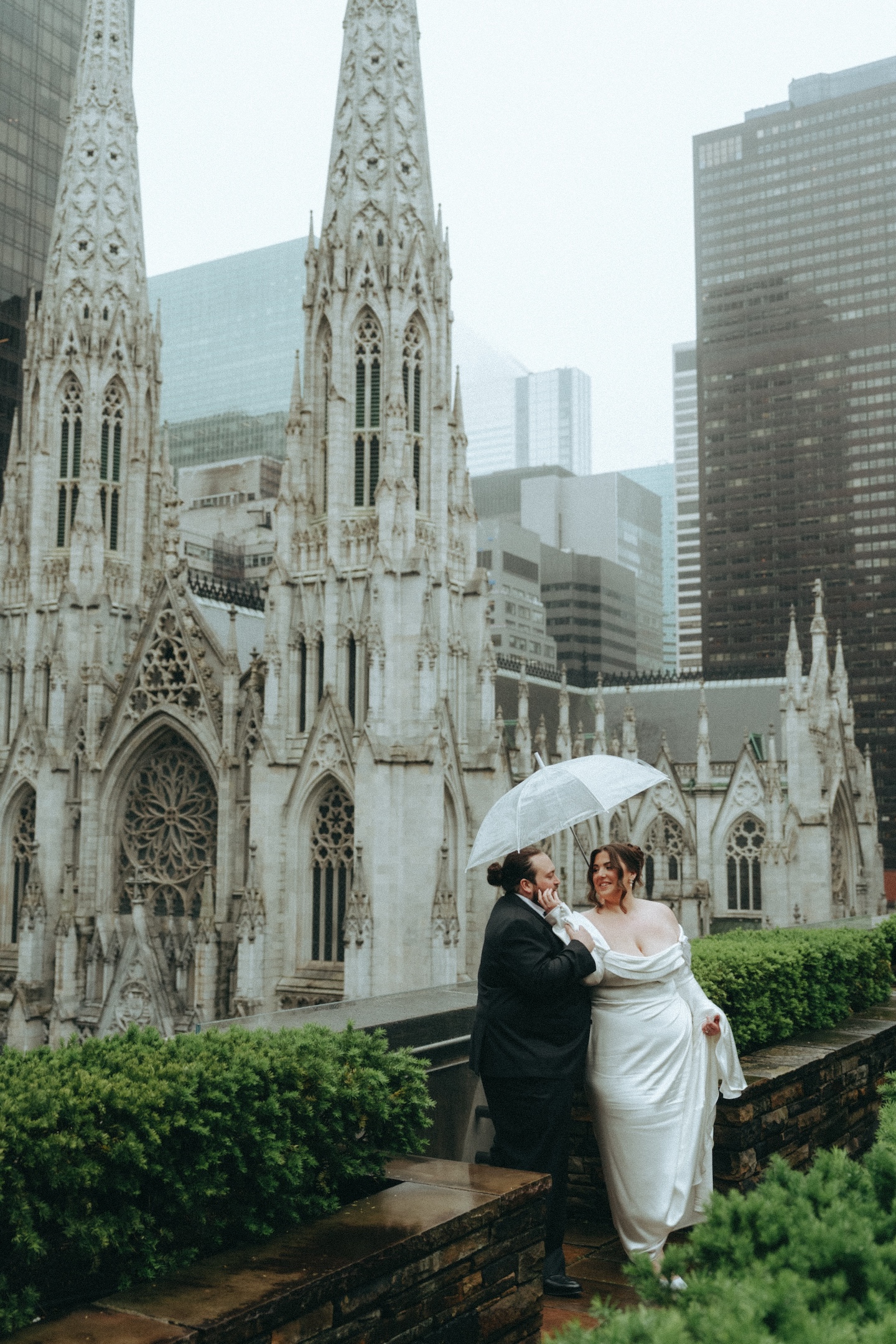 Bride and groom under a clear umbrella by St. Patrick's Cathedral on their rainy NYC elopement day