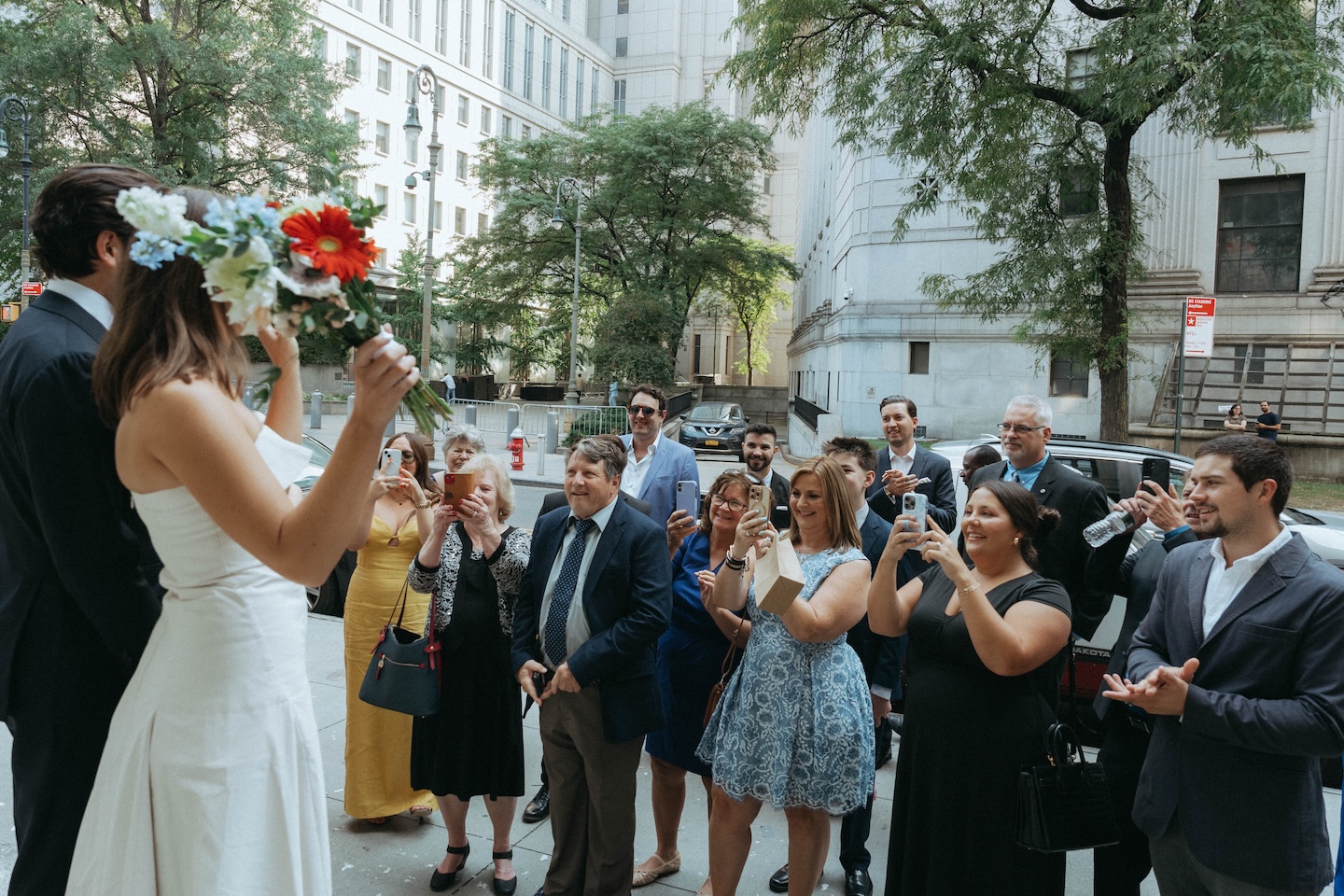 Bride raising her bouquet overhead surrounded by guests on a Manhattan street