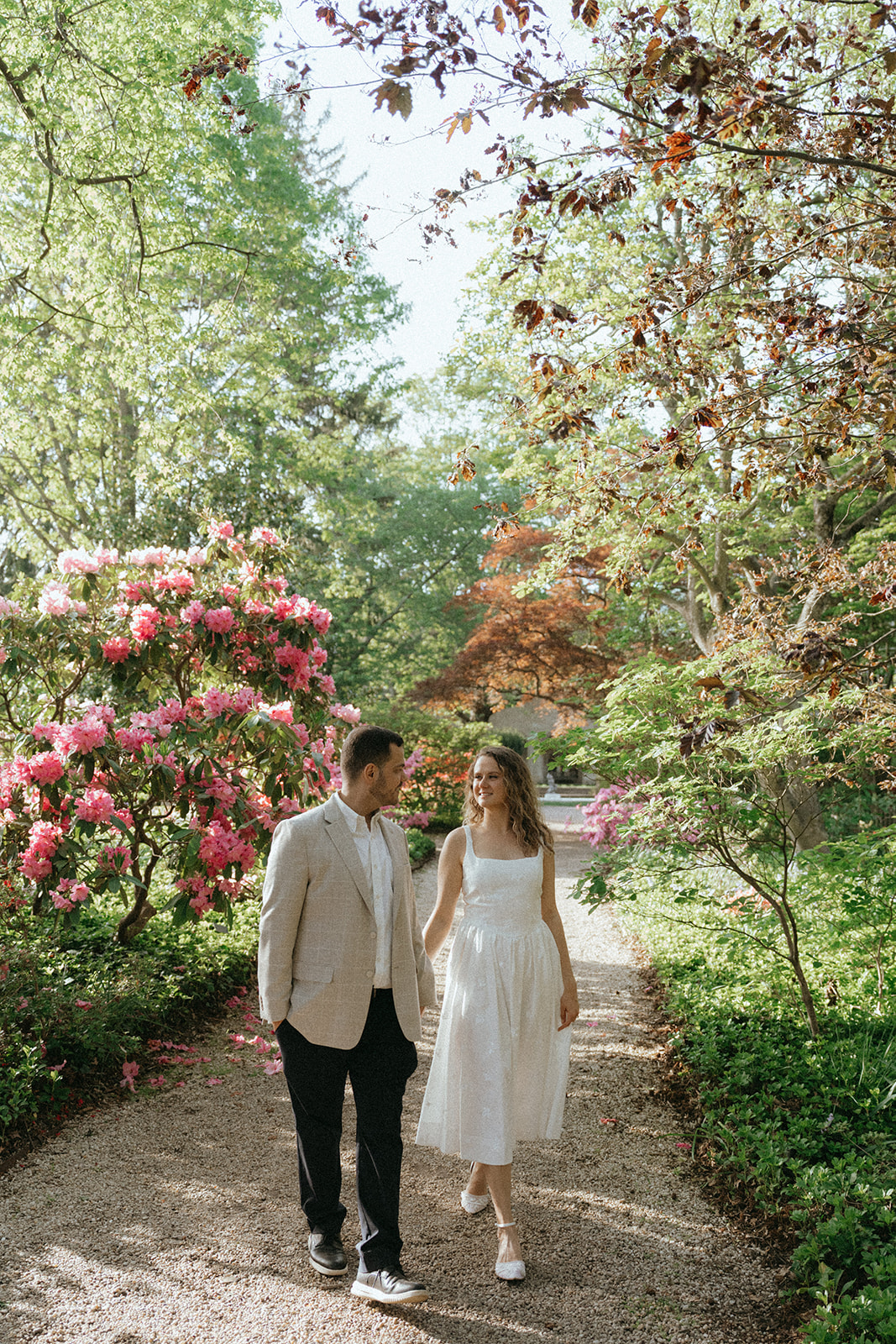 Man and woman walk through floral garden during Planting Fields Arboretum engagement photos