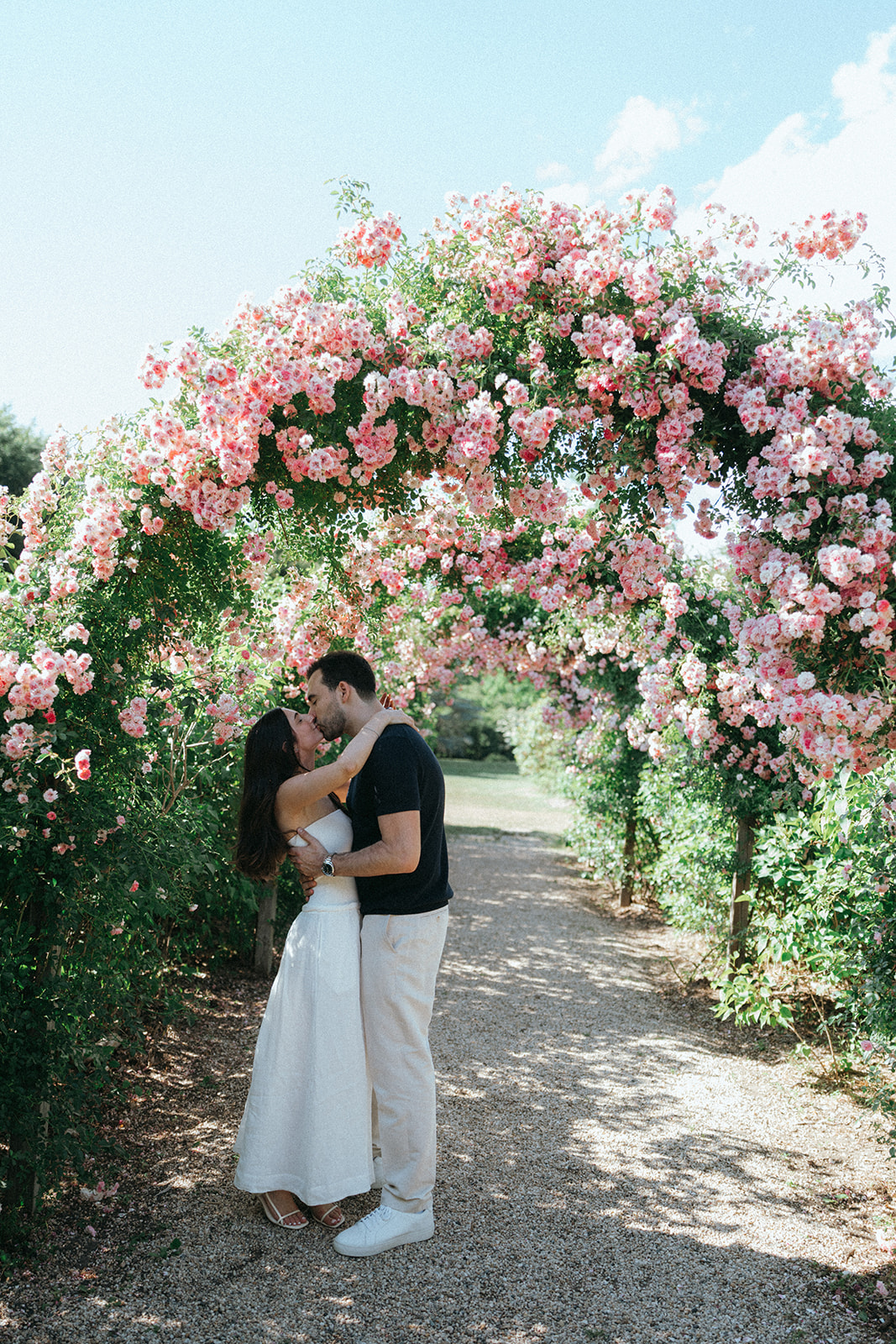 Man and woman kiss under floral arch during Planting Fields Arboretum engagement photos