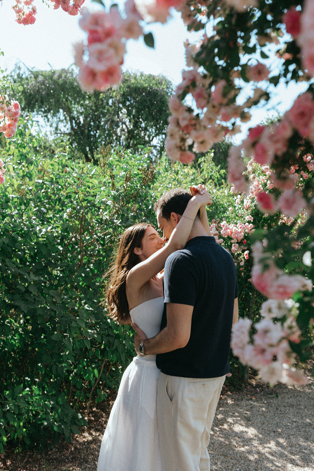 Man and woman embracing under pink flowers during Planting Fields Arboretum engagement photos