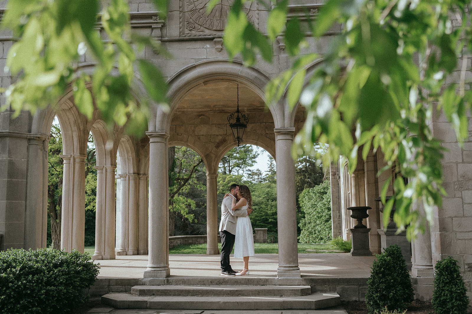 Man and woman kiss under arch after proposal at Planting Fields Arboretum