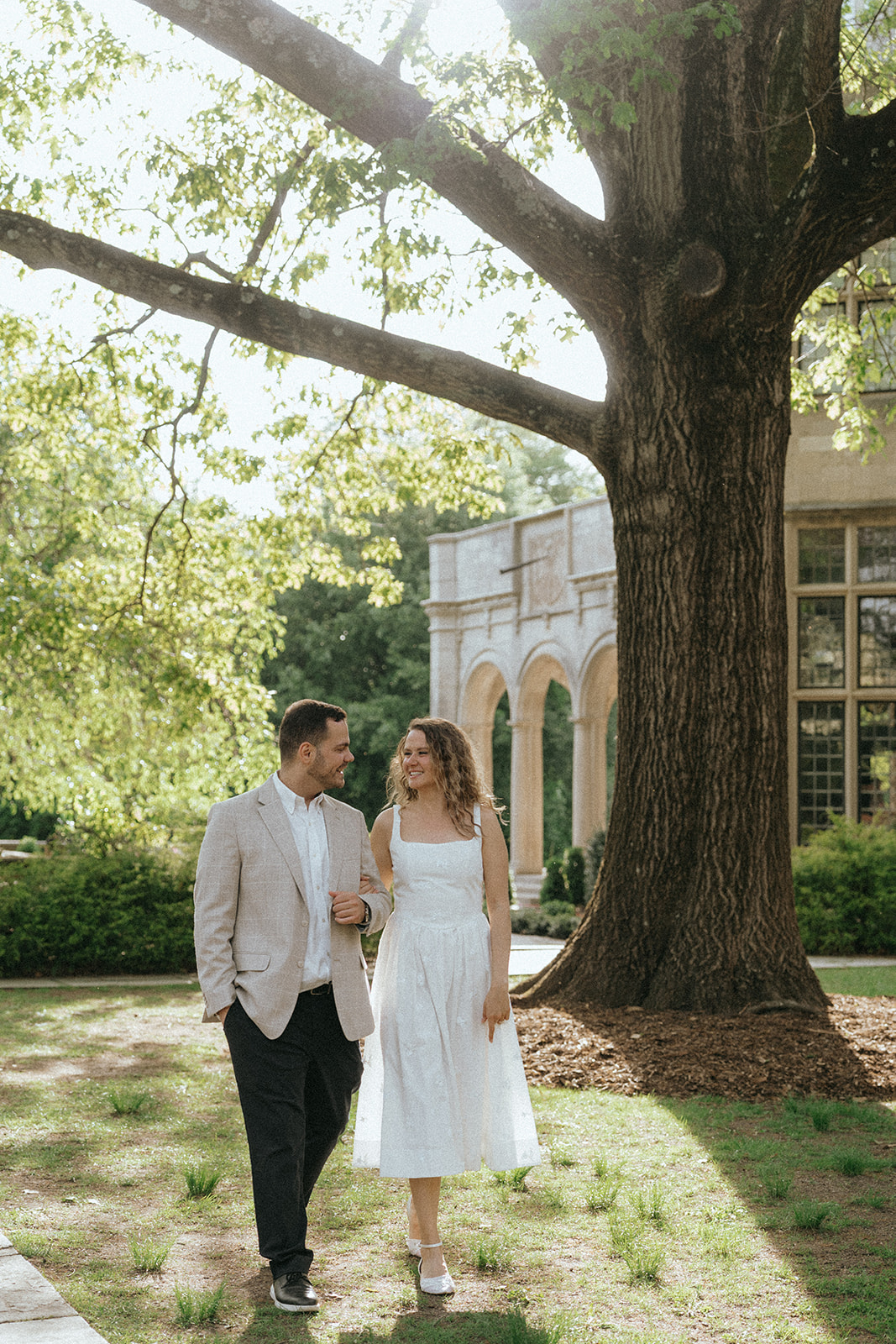 Man and woman walking in sun spot during Planting Fields Arboretum engagement photos