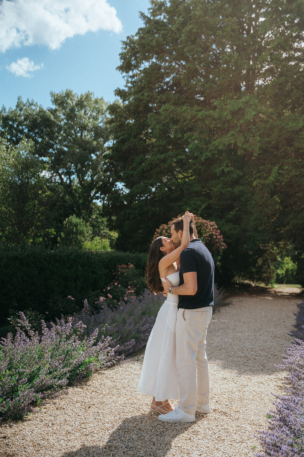 Man and woman in white dress kissing at Planting Fields Arboretum during engagement photos
