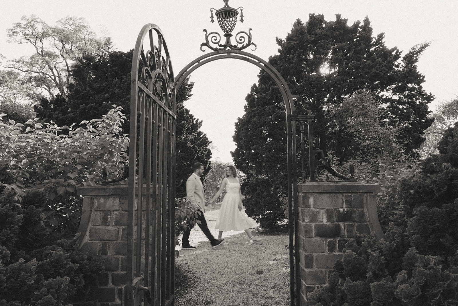 Black and white photo of man and woman walking in Planting Fields Arboretum during engagement photos