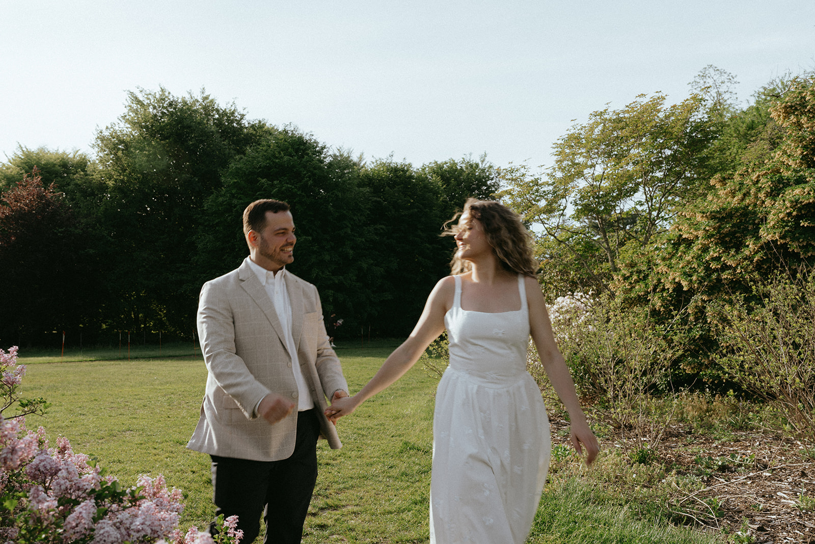 Man and woman walk through field with flowers at Planting Fields Arboretum during engagement photos